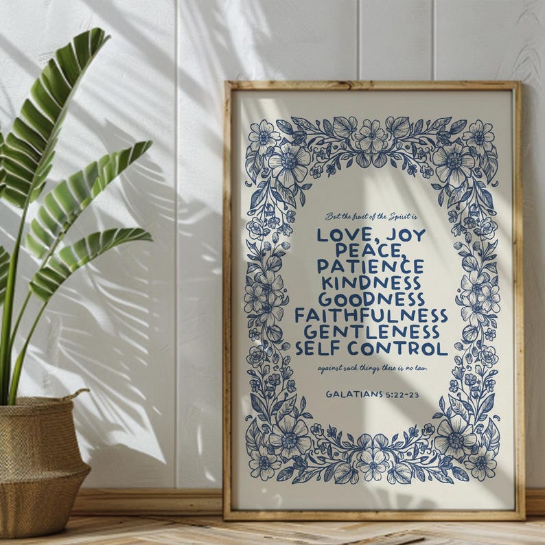 May include: A framed print with a floral border in navy blue. The text reads "But the fruit of the Spirit is LOVE, JOY, PEACE, PATIENCE, KINDNESS, GOODNESS, FAITHFULNESS, GENTLENESS, SELF CONTROL" and "GALATIANS 5:22-23". The frame is a light brown color.