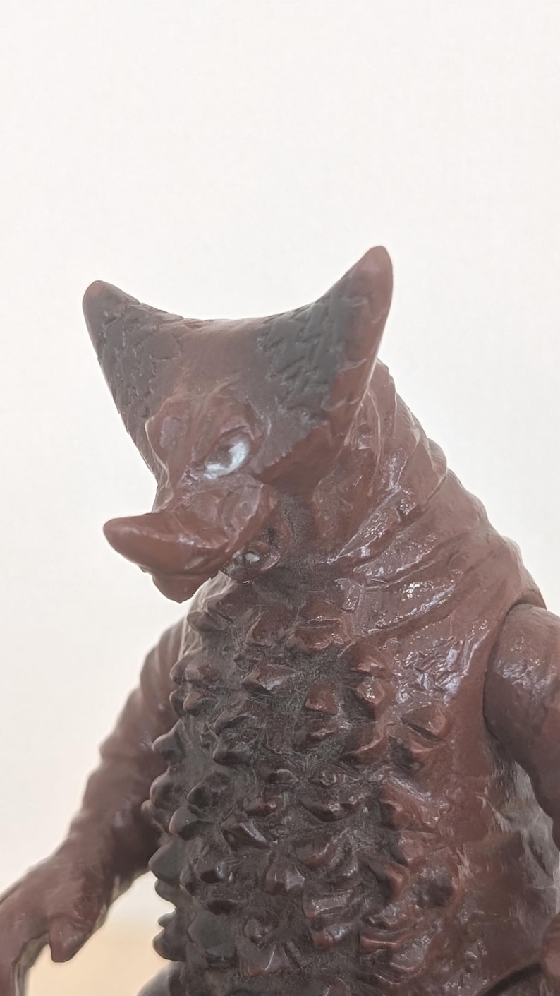 May include: A brown monster figurine with a textured surface and a prominent horn. The figure has a snout and a detailed, rough skin texture. The figurine is a collectible item.