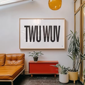 May include: A framed art print with the letters TWU WUV in bold black font. The artwork hangs above a red cabinet, with a brown leather sofa to the left. Potted plants and a yellow pendant light add to the room's decor.