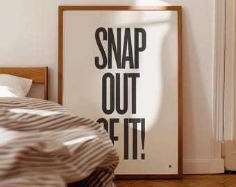 Puede incluir: Un póster enmarcado con las palabras "SNAP OUT OF IT!" en letras negras en negrita. El póster tiene un fondo claro y un marco de madera. El póster se muestra en un dormitorio, con una cama y ropa de cama a rayas visibles.
