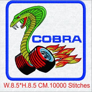 Op de afbeelding: Geborduurde patch met een groene cobra met een rode bek en gele lichaam, boven het woord "COBRA" in blauw. De cobra is gepositioneerd boven twee zwarte en rode banden met vlammen. De patch is 8,5 cm breed en 8,5 cm hoog.