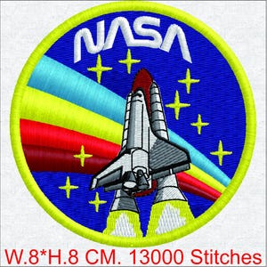 Puede incluir: Parche bordado con el logotipo de la NASA y un diseño de transbordador espacial. El parche es circular, con un fondo azul y un borde amarillo. El texto "NASA" es blanco. El parche mide 8 cm de ancho y 8 cm de alto.