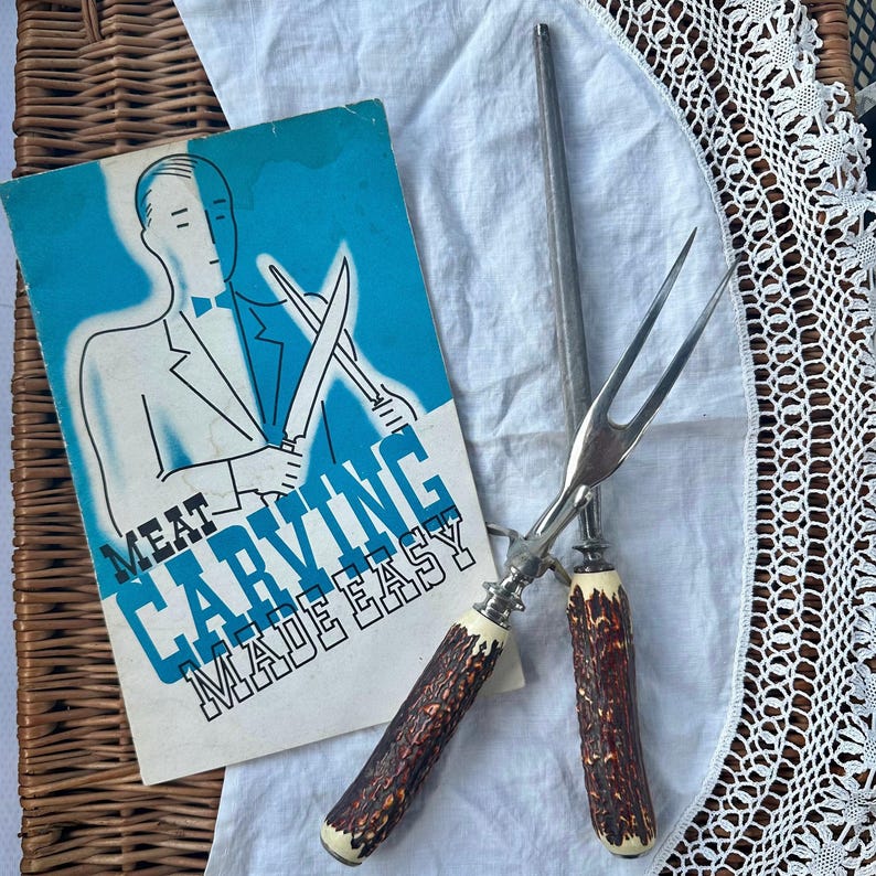 May include: Vintage meat carving set with a sharpening steel and a booklet. The carving fork and knife handles have a brown, textured design with cream-colored accents. The booklet has a blue background with the text "MEAT CARVING MADE EASY."