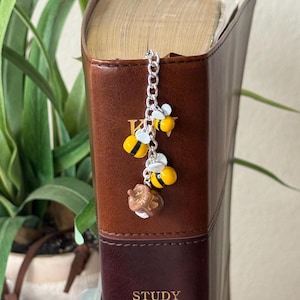 May include: A silver chain bookmark with three charms: two yellow and black bees and a small brown donut. The bookmark is placed in a brown leather-bound Study Bible with the text "STUDY BIBLE" and "KING JAMES" visible.