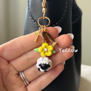 May include: A gold-colored keychain with a cross charm, a brown staff, a yellow flower, and a black and white sheep charm. The word "Yellow" is written in white on the image.