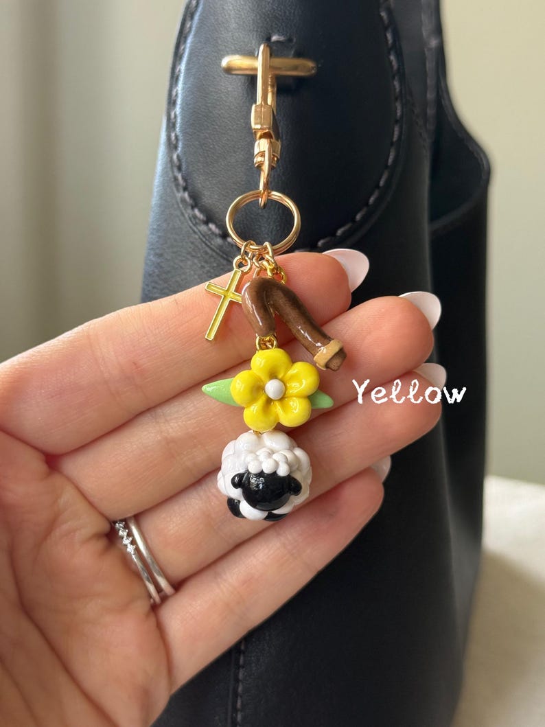 May include: A gold-colored keychain with a cross charm, a brown staff, a yellow flower, and a black and white sheep charm. The word "Yellow" is written in white on the image.