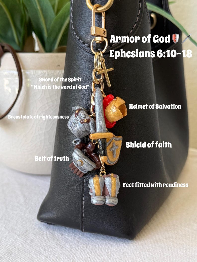 Op de afbeelding: Een goudkleurige metalen sleutelhanger met miniatuurbedels die de wapenrusting van God voorstellen, waaronder een zwaard, helm, schild, borstplaat, riem en laarzen. De tekst Armor of God Ephesians 6:10-18 staat bij de bedels afgebeeld.