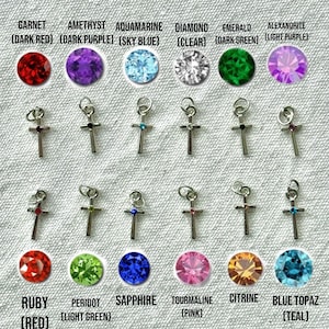 May include: A collection of silver cross pendants with various gemstone accents, including garnet, amethyst, aquamarine, diamond, emerald, alexandrite, ruby, peridot, sapphire, tourmaline, citrine, and blue topaz. Text at the top reads: "CROSS STONES APPEAR DARKER IN PHOTOS - SEE THE LARGER GEMSTONE IMAGES FOR MORE ACCURATE COLOR REFERENCE".