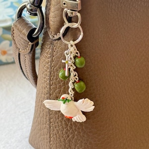 Puede incluir: Un juego de tres tazas de cerámica con un esmalte moteado de color crema. Cada taza presenta un diseño pintado a mano diferente: una hoja azul y verde, una flor amarilla y una baya roja. Las tazas tienen un diseño simple y moderno.