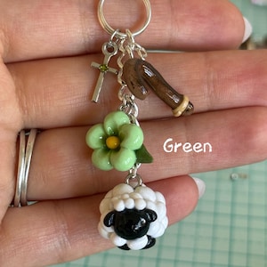May include: A silver keychain with multiple charms. Charms include a cross, a brown horseshoe, a green flower, and a black and white sheep. The word "Green" is written in green text.