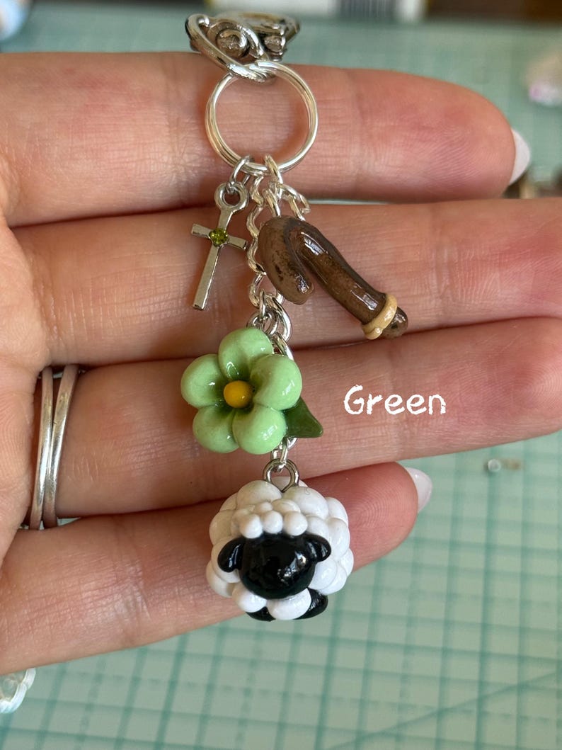 May include: A silver keychain with multiple charms. Charms include a cross, a brown horseshoe, a green flower, and a black and white sheep. The word "Green" is written in green text.