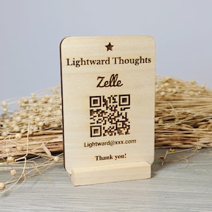 May include: A wooden sign with the text "Lightward Thoughts", "Zelle", a QR code, and the email address "Lightward@xxx.com". The sign is supported by a small wooden stand and has a star at the top. The words "Thank you!" are at the bottom.