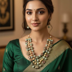Peut inclure: Une femme porte un collier à plusieurs rangs et des boucles d'oreilles assorties. Le collier présente plusieurs rangs d'éléments ronds et perlés dans des tons de vert, d'or et de rouge. Elle porte un haut vert et un vêtement à motifs verts et dorés.