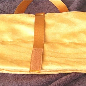 May include: A rectangular, mustard yellow fabric roll-up case featuring a matching yellow nylon strap with a hook-and-loop fastener closure. The case is constructed from a soft, slightly textured material and is shown in a folded, closed position.