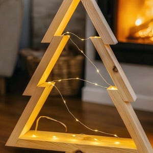 Peut inclure: Décoration de sapin de Noël en bois avec des lumières LED blanc chaud. L'arbre est construit en bois clair et a une forme triangulaire. Les lumières sont réparties dans l'arbre, créant une ambiance chaleureuse et festive. L'arbre est posé sur une surface en bois.