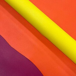 May include: A vibrant assortment of colorful leather sheets. The image showcases a spectrum of hues, including a bright yellow roll, alongside shades of orange, red-orange, and deep purple. The textures appear smooth and slightly textured, ideal for crafting.
