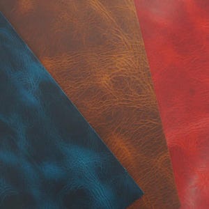Op de afbeelding: Close-up van drie stukken getextureerd leer in tinten blauw, bruin en rood. Het leer heeft een verweerde, vintage uitstraling met zichtbare nerf en subtiele kleurvariaties. De stukken zijn in hoeken gerangschikt en tonen de verschillende kleuren en texturen.