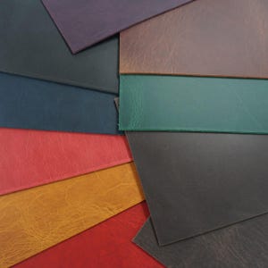 Puede incluir: Una colección de muestras de cuero de colores en varios tonos, incluyendo rojo, dorado, verde y morado. El cuero tiene un aspecto texturizado, con grano visible y sutiles variaciones de color. Las muestras están dispuestas en un patrón superpuesto.