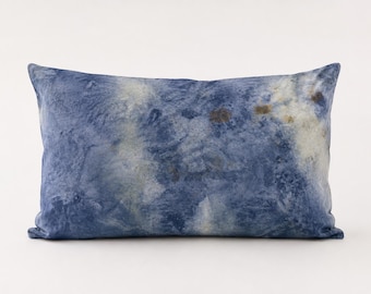 May include: A rectangular decorative pillow with a blue and white marbled pattern. The pillow has a soft, textured appearance, with darker blue hues blending into lighter shades of white and hints of brown. The pillow is designed for home decor.
