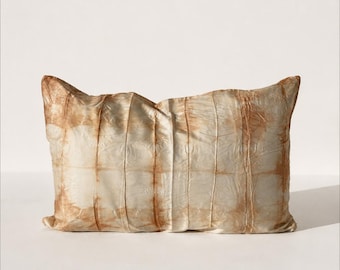 May include: A rectangular throw pillow featuring a cream-colored base with a grid-like pattern of vertical and horizontal lines in shades of light brown. The fabric has a crinkled, textured appearance with subtle variations in color intensity.