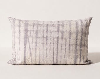 May include: A rectangular throw pillow featuring a tie-dye pattern with vertical and horizontal lines in shades of muted grey and off-white. The fabric has a textured, crinkled appearance with soft, blurred edges where the grey dye meets the white.