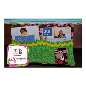 May include: A green fabric organizer with pockets for books and a small pocket for headphones. The organizer has a yellow wavy trim and a pink and green floral print. The text "PB teen" is visible on one of the books.