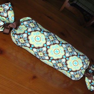 May include: A brown, blue, and green patterned fabric bolster pillow with a bow at each end.