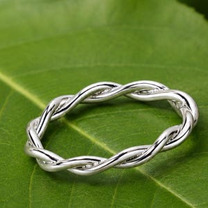 Op de afbeelding: Een ring van gepolijst zilver met een doorlopend gedraaid touwontwerp. De band is opgebouwd uit twee in elkaar gevlochten metalen strengen die een getextureerd, gevlochten uiterlijk creëren over de gehele omtrek van het ronde sieraad.