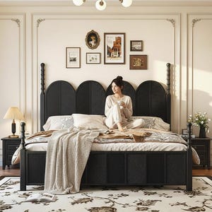 Può includere: Un letto nero con testiera e pediera intrecciate. Il letto è fatto con biancheria da letto bianca e una coperta beige. Un tappeto floreale è sotto il letto. Una donna è seduta sul letto.