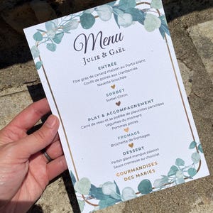 Peut inclure: Une carte de menu de mariage rectangulaire avec un fond blanc, une bordure dorée et des feuilles d'eucalyptus à l'aquarelle. Le texte indique Menu, Julie & Gaël, Entrée, Sorbet, Plat & Accompagnement, Fromage, Dessert et Gourmandises des Mariés.
