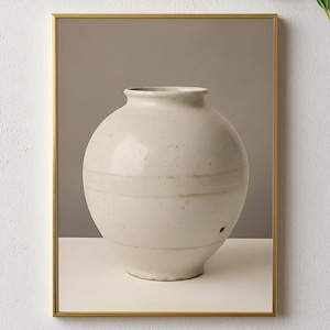 Puede incluir: Imagen enmarcada de un jarrón de cerámica moteada, de color blanquecino, con cuerpo redondeado y cuello estrecho. El jarrón tiene bandas horizontales y se apoya sobre una superficie blanca sobre un fondo neutro. El marco es dorado.