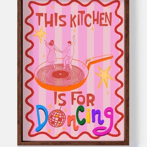May include: A framed art print with a pink background and the words "THIS KITCHEN IS FOR Dancing". The image features a couple dancing on a frying pan, with a disco ball and star accents. The artwork has a whimsical, retro style.