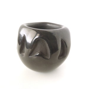 May include: A black ceramic pot with a smooth, shiny finish and a geometric design. The pot is round and has a wide opening.