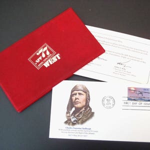 May include: A red commemorative envelope with the text "NPF 77 WEST" in white. An envelope with a portrait of Charles Lindbergh and a "First Day of Issue" stamp is also visible, along with a white document.