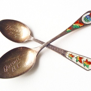 May include: Two silver spoons with engraved text "Queen  El." One spoon has a painted design of maple leaves and the word "Canada" on the handle.