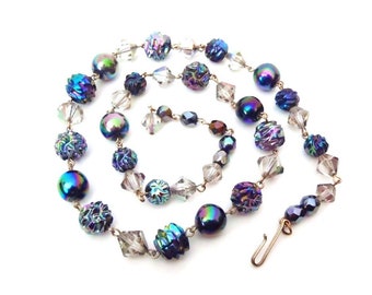 May include: A vintage iridescent necklace with a mix of clear and dark blue glass beads. The necklace features a variety of bead shapes, including round, faceted, and textured.