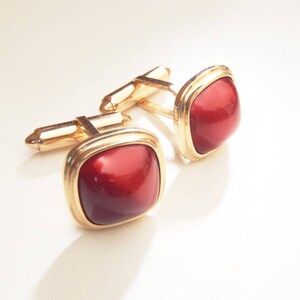 May include: A pair of gold cufflinks with red gemstone accents. The cufflinks have a square shape and a polished finish.