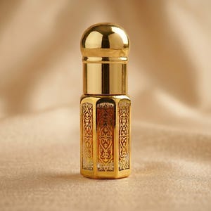 May include: A small, ornate gold perfume bottle with a rounded top and a decorative, patterned design. The bottle is made of gold-colored metal and has a clear glass interior. The bottle is approximately 3 inches tall.