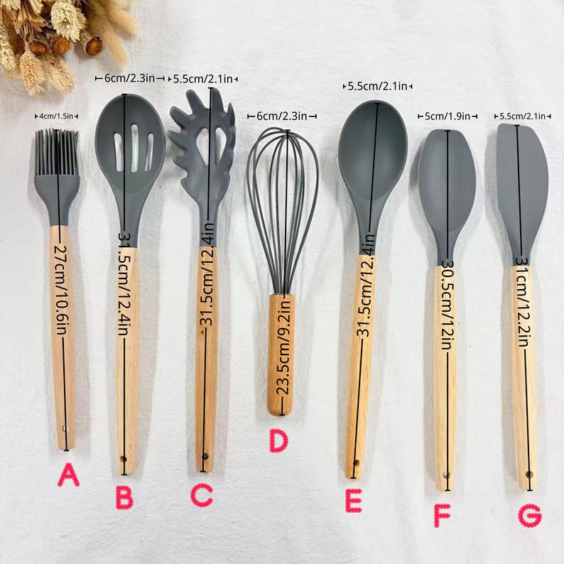 May include: A set of seven kitchen utensils with gray silicone heads and natural wood handles. The set includes a basting brush, slotted spoon, pasta server, whisk, spoon, spatula, and a solid spoon. The utensils range from 10.6 inches to 12.4 inches in length.