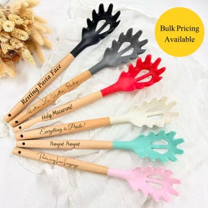 May include: Six pasta spoons with wooden handles and colourful silicone heads. Each spoon has a different colour head and an engraved phrase on the handle, including "Resting Pasta Face" and "Holy Macaroni!"