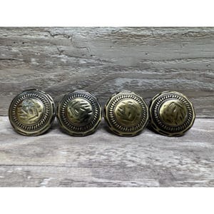 May include: Four antique brass cabinet knobs with a circular design. Each knob features a central leaf pattern surrounded by a detailed border. The knobs are arranged in a row on a wooden surface.