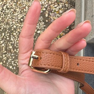 Close-up of gold buckle and stitching on adjustable strap of brown clear crossbody bag