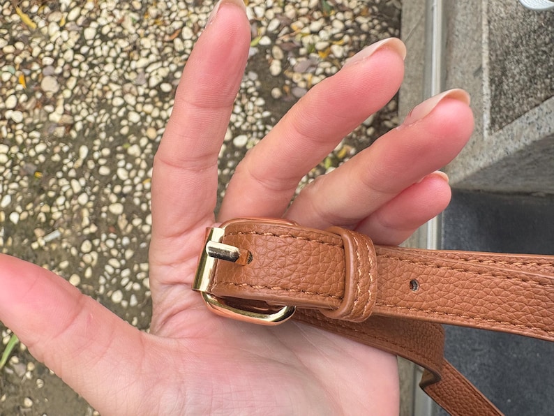 Close-up of gold buckle and stitching on adjustable strap of brown clear crossbody bag