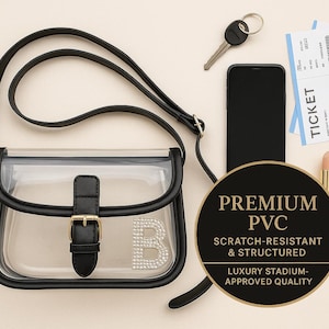 May include: A clear PVC crossbody bag with black trim, a black strap, and a gold buckle. The bag has a rhinestone "B" on the front. Other items include a phone, keys, tickets, and lipstick. A black circle reads "PREMIUM PVC".