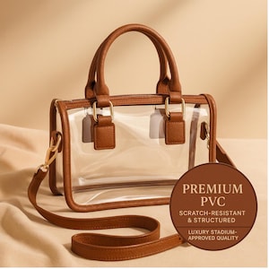 May include: Transparent PVC handbag with brown leather detailing, including handles and a shoulder strap. The bag features gold-tone hardware and a circular label stating "PREMIUM PVC, SCRATCH-RESISTANT & STRUCTURED, LUXURY STADIUM-APPROVED QUALITY."