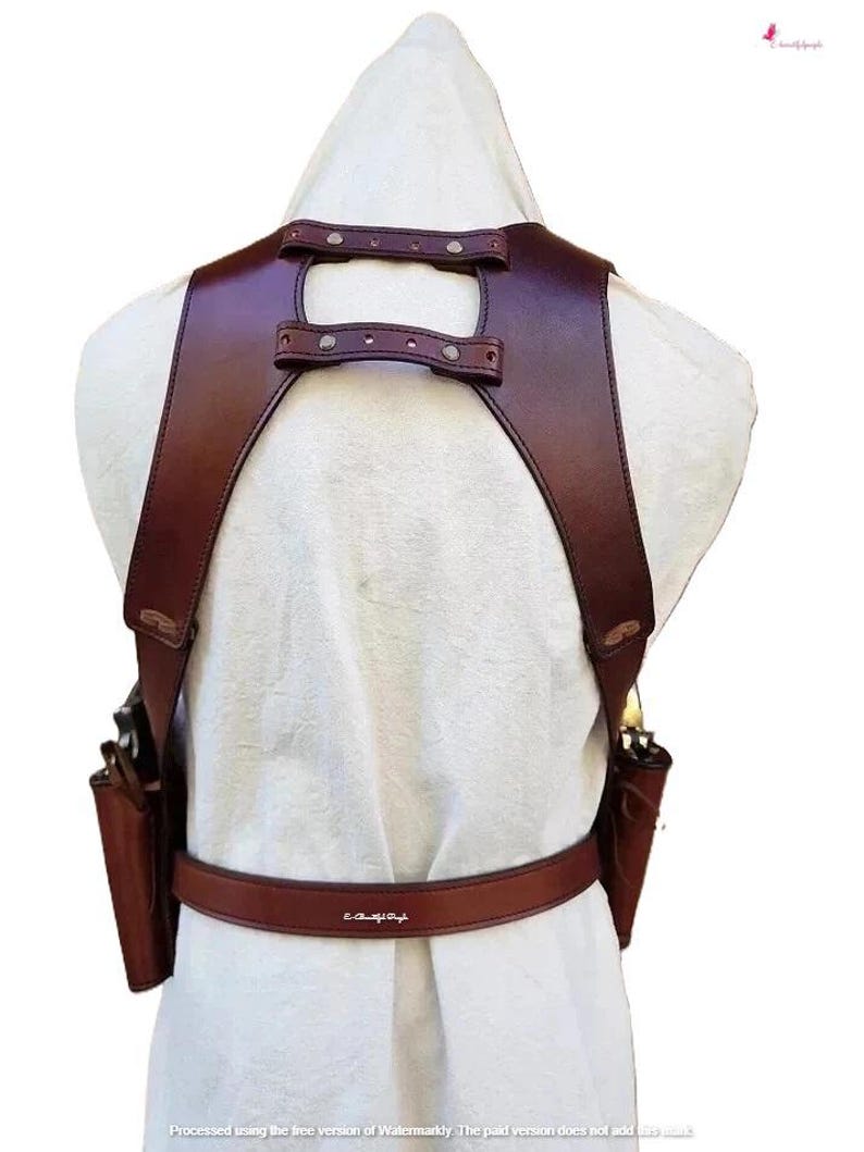 K&ouml;nnte beinhalten: Ein braunes Leder-Schulterholster mit zwei angebrachten Taschen und einem G&uuml;rtel. Das Holster verf&uuml;gt &uuml;ber verstellbare Riemen und Metallnieten. Das Design ist von hinten sichtbar und zeigt die Handwerkskunst und die Details.