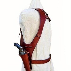 K&ouml;nnte beinhalten: Ein braunes Schulterholster aus Leder mit passendem G&uuml;rtel. Das Holster ist f&uuml;r eine Schusswaffe konzipiert, mit sichtbarem Lauf und Griff. Das Leder hat eine satte, rotbraune Farbe.
