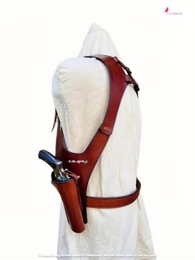 K&ouml;nnte beinhalten: Ein braunes Schulterholster aus Leder mit passendem G&uuml;rtel. Das Holster ist f&uuml;r eine Schusswaffe konzipiert, mit sichtbarem Lauf und Griff. Das Leder hat eine satte, rotbraune Farbe.
