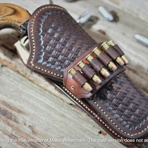Op de afbeelding: Een bruin leren holster met een geweven patroon, met een revolver met een houten handvat. De holster heeft een riem voor kogels. De afbeelding staat op een houten oppervlak.