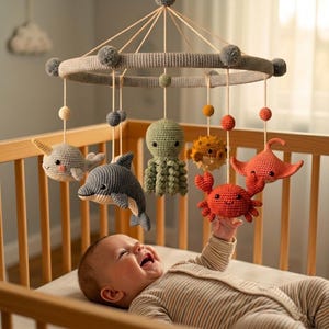 May include: A circular crochet baby mobile featuring a grey ring with pom-poms, suspending various stuffed sea creatures including a narwhal, dolphin, octopus, pufferfish, crab, and stingray, all crafted in colorful yarn with detailed stitching.